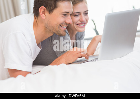 Happy couple in bed using notebook and smiling Stock Photo - Alamy