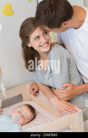 Happy parents watching over baby son in crib Stock Photo