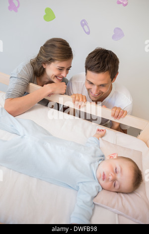 Happy parents watching over baby son in crib Stock Photo