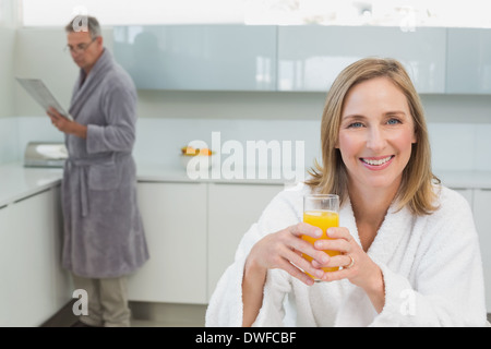 Smiling woman holding orange juice with man in background Stock Photo