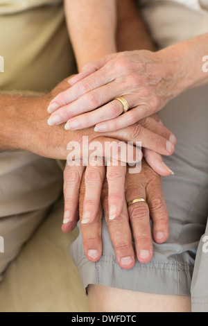 Senior couple sitting on couch holding hands Stock Photo