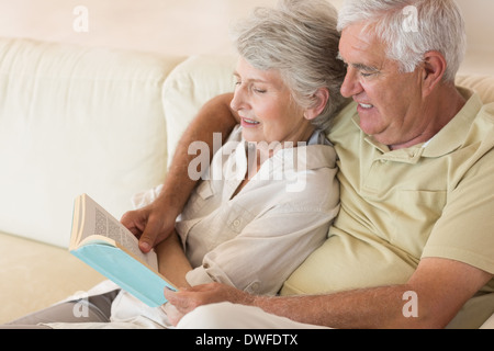 Senior couple sitting on couch reading together Stock Photo