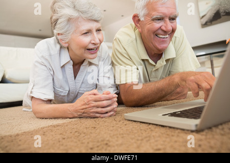Cheerful senior couple using the laptop together lying on rug Stock Photo