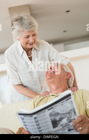 Senior man reading newspaper with partner leaning on shoulders Stock Photo