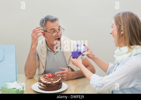 Shocked man receiving a gift by cake on table Stock Photo