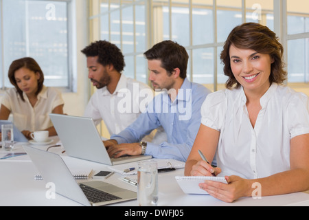 Smiling businesswoman writing notes with colleagues in meeting at office Stock Photo
