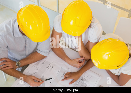 Architects in yellow helmets working on blueprints at office Stock Photo