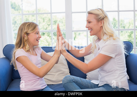 Happy mother and daughter playing clapping game on sofa Stock Photo