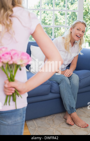 Mother looking at girl hiding flowers behind back Stock Photo