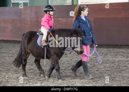 A four year old girl riding a pony during a riding lesson in North Lincolnshire, England, 2014 Stock Photo