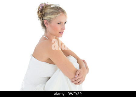 Thoughtful bride hugging knees over white background Stock Photo