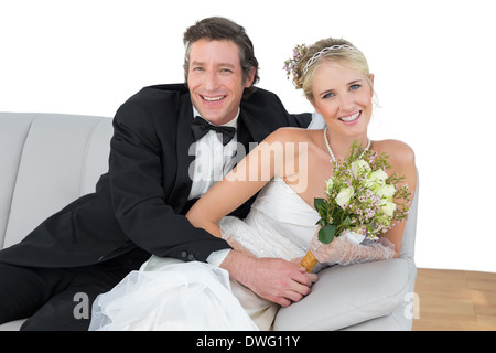 Bride and groom with flower bouquet sitting on sofa Stock Photo
