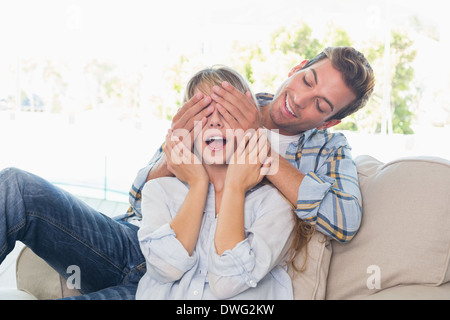 Man covering happy womans eyes in living room Stock Photo