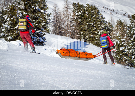 Two members of a ski patrol helping an injured skier down the mountain. Stock Photo