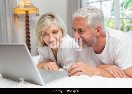 Happy mature couple using laptop in bed Stock Photo