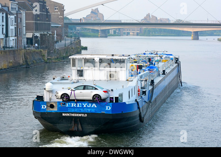 Maastricht Limburg commercial transport on River Meuse (River Maas) motor barge travels along urban landscape loaded with assumed crew member own car Stock Photo