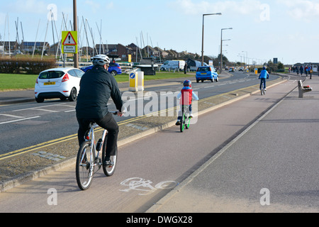 Father and son sunny winter day bike riders on two way dedicated roadside cycle lane beside seafront road traffic at Southend on Sea Essex England UK Stock Photo