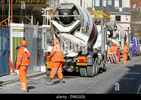 Traffic Marshalls on building construction site supervise traffic flow for concrete cement lorry trucks unloading by crane on public highway London UK Stock Photo