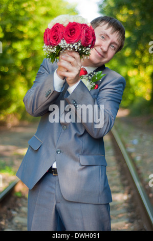 the beautiful young groom with a bouquet of red-white roses on a track in the summer Stock Photo