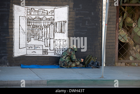 Homeless man sitting on sidewalk next to mural of clothes closet, East Village, San Diego, California Stock Photo