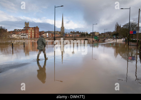 A photograph of the River Severn flooding over Tybridge Street in Worcester as a pedestrian tries to cross on foot. Stock Photo