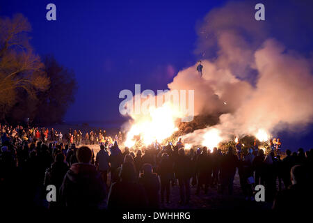 Langenargen, Germany. 08th Mar, 2014. People stand in around a bonfire on the shores of Lake Constance in Langenargen, Germany, 08 March 2014. Hundreds of people attended the spectator. The bonfire itself is made up of ten meter stack of around 800 Christmas trees which the Langenargen fire department set up. Photo: FELIX KAESTLE/dpa/Alamy Live News Stock Photo