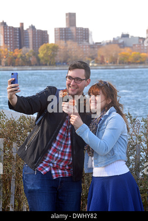 A young couple at a food fair in Williamsburg Brooklyn taking selfies with the Manhattan skyline behind them. Stock Photo
