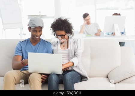 Couple using laptop with colleagues in background at creative office Stock Photo