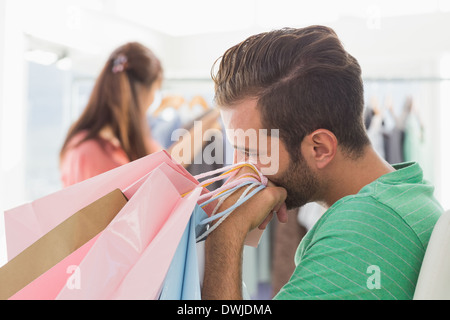 Bored man with shopping bags while woman by clothes rack Stock Photo
