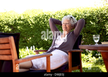 Senior woman sitting on a chair and taking a nap in backyard. Elder woman sleeping in backyard garden Stock Photo