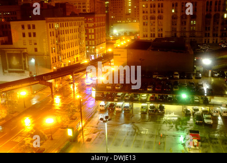 Chicago night. The El train track runs above a sodium lit street past a rain soaked multi story car park Stock Photo