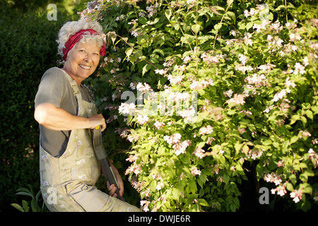 Portrait of active senior woman digging soil with shovel in garden. Elder woman working with gardening tools in backyard