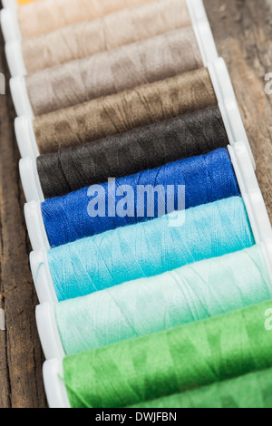 Single row made of color spools of sewing threads, on wooden background Stock Photo