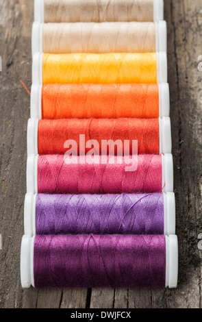 Single row made of color spools of sewing threads, on wooden background Stock Photo