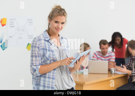 Smiling young designer using her tablet pc in front of her colleagues Stock Photo