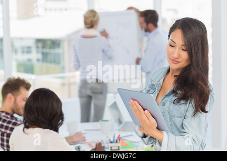 Asian woman using her tablet pc while her colleagues are working Stock Photo