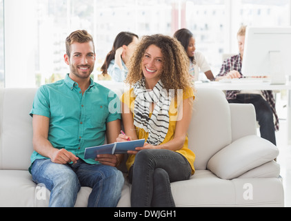 Smiling designers working together on the couch looking at camera Stock Photo