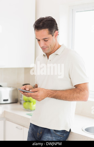 Side view of a man text messaging in kitchen Stock Photo