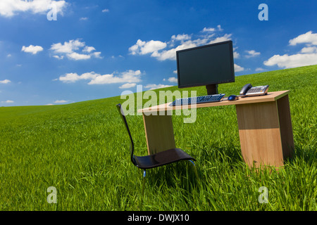 Business concept shot showing a computer on a desk in a green field with a blue sky and white clouds Stock Photo