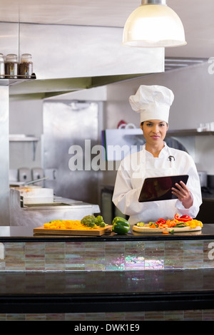 Female chef using digital tablet while cutting vegetables in kitchen Stock Photo