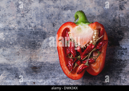 Half of raw red pepper stuffed by little red hot chili peppers over vintage background. Stock Photo