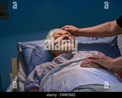 Contented smiling senior old age elderly lady in hospital bed at night with comforting hand of carer nurse Stock Photo