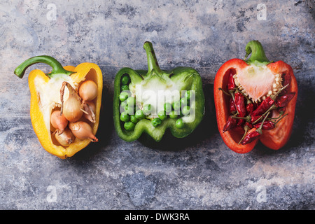 Half of raw red, green and yellow peppers stuffed by little onions, peas and red hot chili peppers over vintage background. Stock Photo