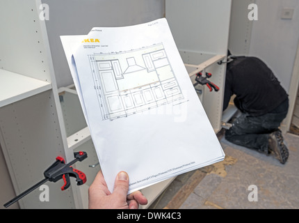 Man holding Ikea kitchen plan with worker installing kitchen in the background Stock Photo