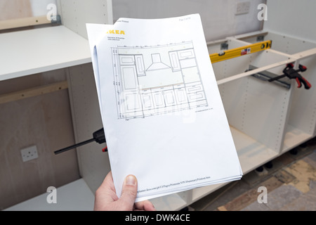 Man holding Ikea kitchen plan with half built kitchen in the background Stock Photo