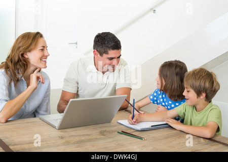 Parents with laptop assisting children coloring Stock Photo