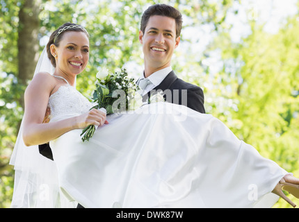 Groom carrying bride in garden Stock Photo