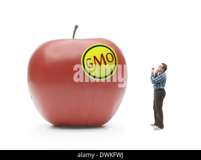 Man holding natural organic apple being bewildered when standing and looking at giant GMO-modified red apple shot on white Stock Photo