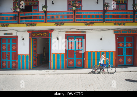 Boy walks his bike past colorful architecture next to Jardin's plaza, Jardin, Antioquia, Colombia, South America Stock Photo