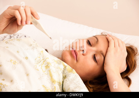 woman checking fever with digital termomether girl with flu resting in bed Stock Photo